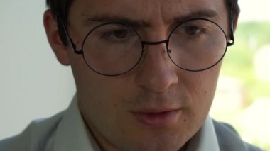 Gömlekli bir adam yuvarlak gözlüklerini düzeltir.