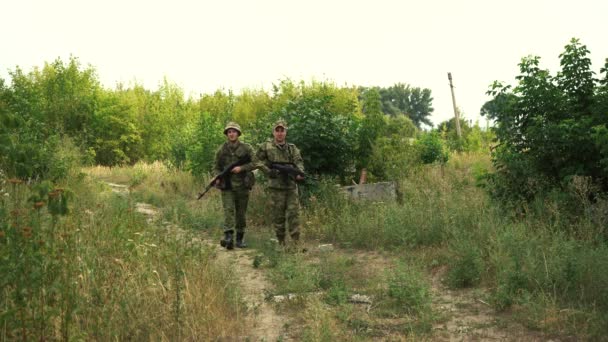 Dois soldados em camuflagem com armas estão caminhando por uma área florestal — Vídeo de Stock