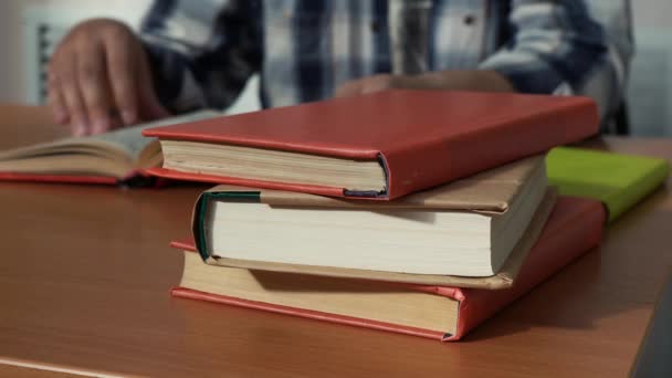 Uma pilha de livros deitados na mesa de um homem que lê na biblioteca — Vídeo de Stock