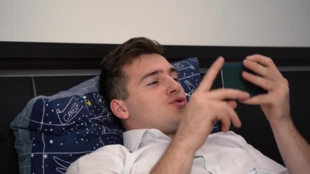 Un bărbat folosește telefonul în timp ce stă culcat pe canapea și este indignat emoțional — Videoclip de stoc