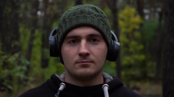 Πορτρέτο ενός άνδρα αθλητή κοιτάζοντας την κάμερα στη μέση του δάσους σε ένα καπέλο και ακουστικά. — Αρχείο Βίντεο