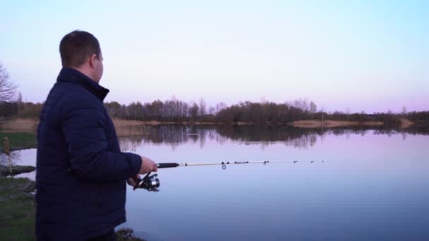 Um homem pescando em pé junto ao lago — Vídeo de Stock