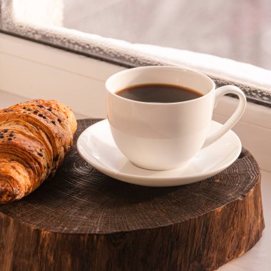 Samimi bir konsept. Klasik kış kahvaltısı. Pencere kenarında bir fincan kahve ve kruvasan standı..