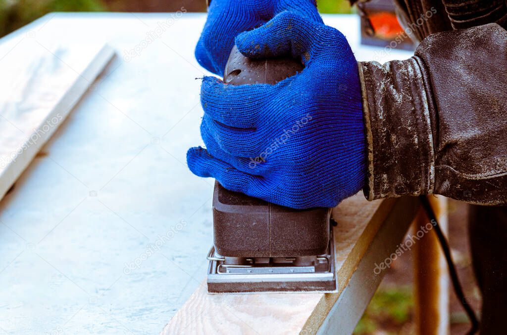 Working with a grind machine. Men's hands in blue gloves work with power tools