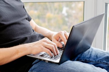 Bilgisayarlı serbest çalışan biri panoramik pencerenin yanındaki ofiste çalışıyor. Erkek ellerine yakın dur.