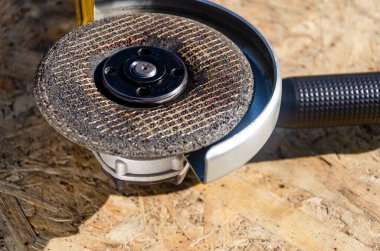 Çalışma masasındaki elektrikli öğütücü kullanılmaya hazır. Ağır endüstri işçisi araba servisinde çeliği yontuyor.