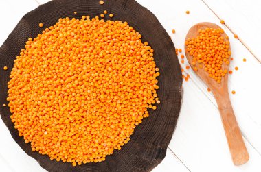 Siyah ahşap bir tabakta kırmızı mercimek ve bulgur ve tahta bir kaşık fotokopi alanı olan beyaz bir tahta masada duruyor. Hasat konsepti