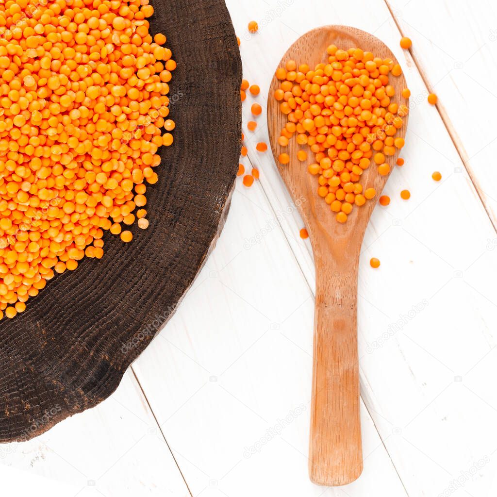 Red lentils and bulgur on a dark wooden plate and a wooden spoon standing on a white wooden table with copy space. Harvest concept