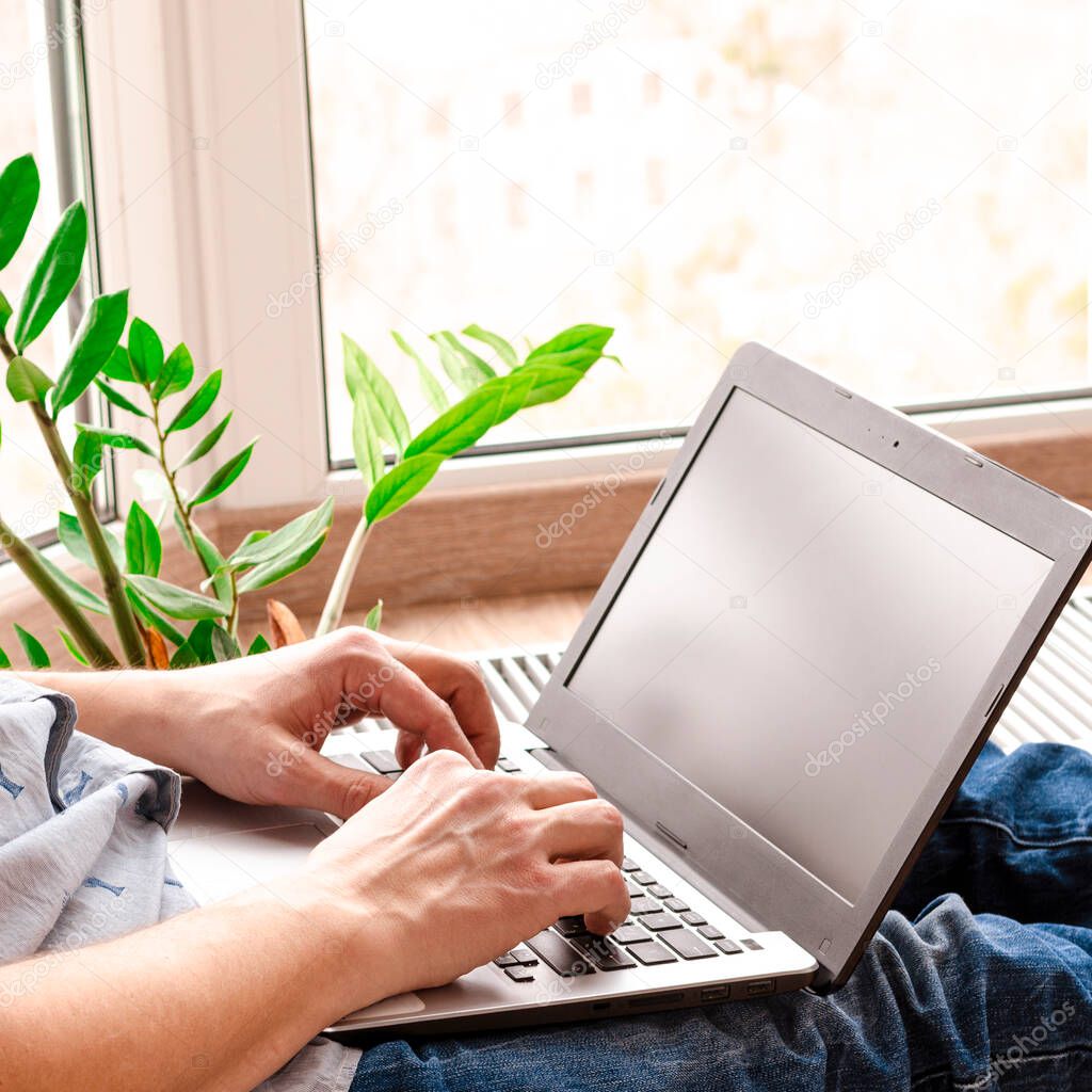 Close up low angle view of a man working from home on a laptop computer sitting at a desk surfing the internet. Remote working from home. Freelancer workplace in kitchen with laptop