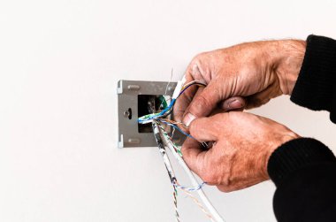 Yaşlı bir adamın elleri, beyaz bir duvara bir roset asıyor. Dairenin tamiri. İnternet