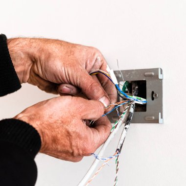 Yaşlı bir adamın elleri, beyaz bir duvara bir roset asıyor. Dairenin tamiri. İnternet