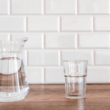 Mutfakta boş bir bardak ve bir sürahi su tezgahı beyaz fayanslardan oluşan bir zemine karşı..