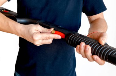 Adamın silahının şarjörüne kırmızı bir av tüfeği kovanını doldurduğu yakın plan. Pompayı şarj ediyorum.