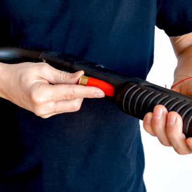 Adamın silahının şarjörüne kırmızı bir av tüfeği kovanını doldurduğu yakın plan. Pompayı şarj ediyorum.