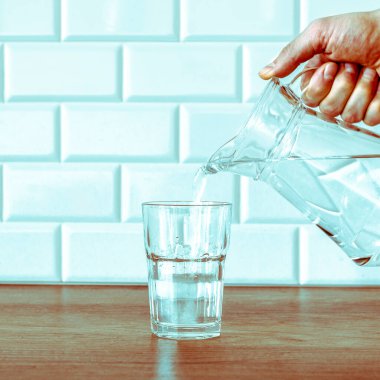 Tahta masadaki cam sürahide arıtılmış tatlı su dökülüyor.