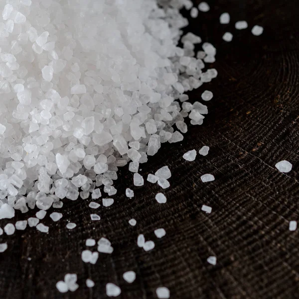 White large crystals of salt scattered on a wooden background