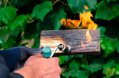 Bir adam gaz ocağından çıkan ateşle tahtaları yakıyor. Tahtanın güzel dokusunu ortaya çıkarmak için ahşap işleme.