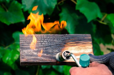 Bir adam gaz ocağından çıkan ateşle tahtaları yakıyor. Tahtanın güzel dokusunu ortaya çıkarmak için ahşap işleme.