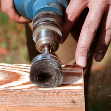 Tahta için tel fırça, bir matkap üzerinde çalışıyor. Erkek el fırçalama makinesini tutuyor. Metal disk ile bir tahta parçasını zımparalıyor..