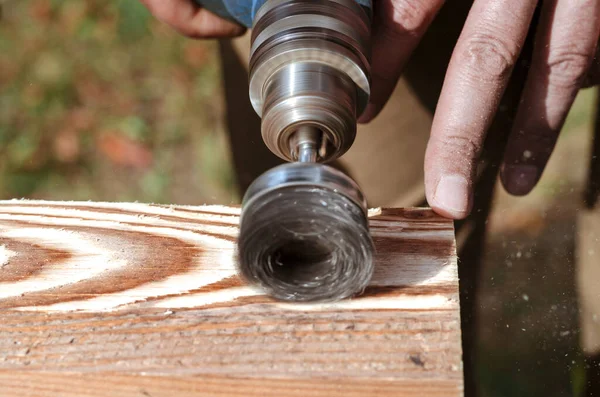 Wire brush for wood working, on a drill. Male hand is holding brushing machine electrical rotating with metal disk sanding a piece of wood.