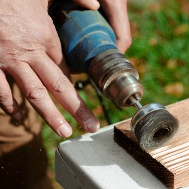 Erkek el fırçalama makinesini tutuyor. Metal disk ile bir tahta parçasını zımparalıyor..