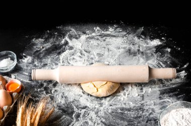 Pizza pişirmek için gerekli malzemeler siyah bir masada yatıyor. Un, hamur, yumurta, kulak