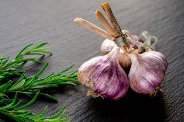 Yemek pişirmek için baharatlar. Siyah arka planda sarımsak ve biberiye var.