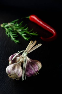 Yemek pişirmek için baharatlar. Siyah arka planda bir demet sarımsak, rormarin ve kırmızı biberlerin yanında.