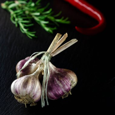 Yemek pişirmek için baharatlar. Siyah arka planda bir demet sarımsak, rormarin ve kırmızı biberlerin yanında.