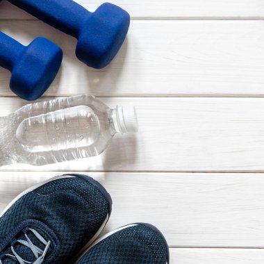 Spor ayakkabıları, dambıllar, bir şişe su ve terazi beyaz arka planda duruyor. Fitness ayarlandı