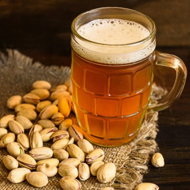 Tahta bir masada bir bardak bira ve fıstık. Kapat..