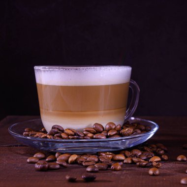Sütlü kahve fincanı ve koyu kahve çekirdeği. Sıcak latte ya da kapuçino Tahta bir masada sütle yapılır.