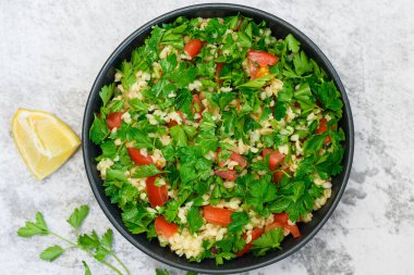 Bulgur ile Tabbouleh salata, maydanoz, bahar soğan ve domates gri arka planda kase. Üst görünüm.