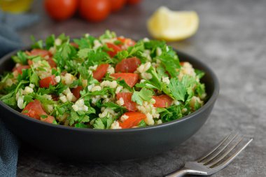 Bulgur, maydanozlu Tabbouleh salatası, yeşil arka planda taze soğan ve domates. Yan görünüm.