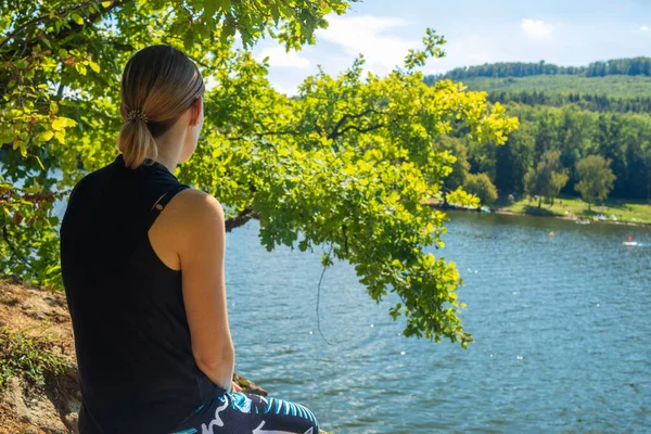 Beauty of a young woman from behind sitting on a rock by the lake. Relax and meditation by the water.