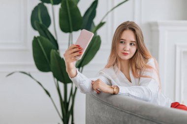 Genç bir kadın selfie çekiyor, akıllı telefondan fotoğraf çekiliyor. Nüfuzlu blogcu sosyal medya ve blog için içerik oluşturur. İç mekanda yaşam tarzı kavramı.
