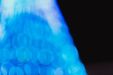 Noel ağacının soyut koyu arkaplanı. Yumuşak bulanık çelenk ışığı mavi tonlarda büyük bir bokeh şeklinde.