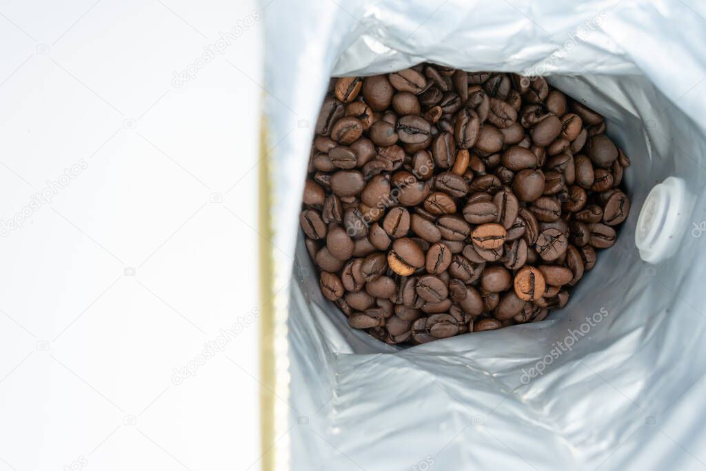 Opened pack of freshly roasted aromatic coffee beans. White background with space for writing. View from above.