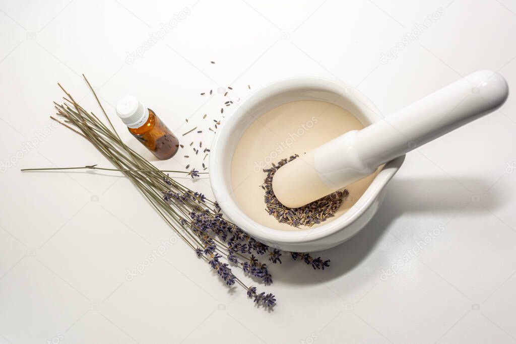 Lavender seeds in a white mortar bowl and a dry lavender bouquet near the oil jar. Cosmetic set, alternative medicine.