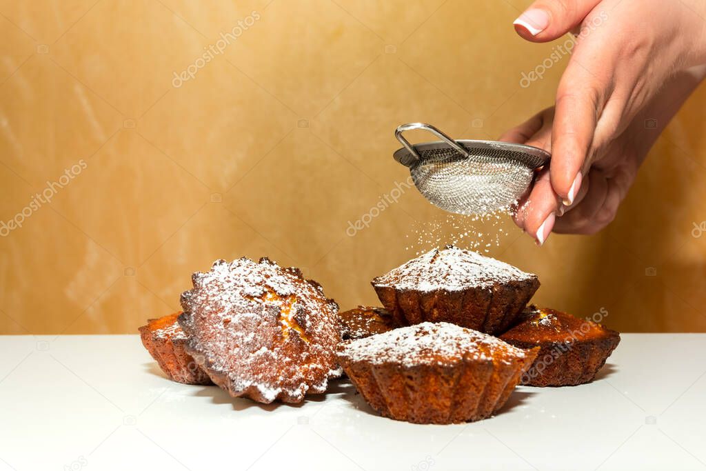 A woman sprinkles sweet cupcakes with powdered sugar on a white table. Homemade baking. Cooking.