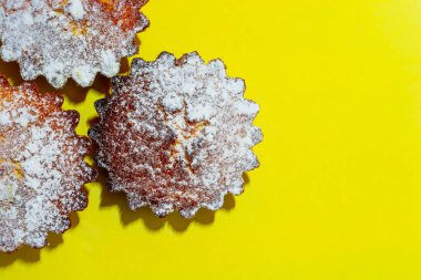 Sarı zemin üzerine pudra şekeri serpiştirilmiş taze pişmiş kekler. Yukarıdan bak. Mutfak teması.