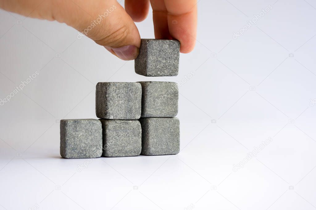 Hand laying stone cubes in the form of a stepped staircase shape, business growth and management concept.