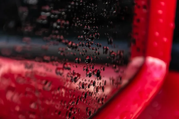 Water drops on a red car mirror close-up. Abstraction.
