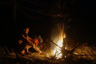 Sakhalin, Rusya - 17 Ekim 2020: Yürüyüşçü Tayga 'daki ateşin yanında kendini ısıtıyor