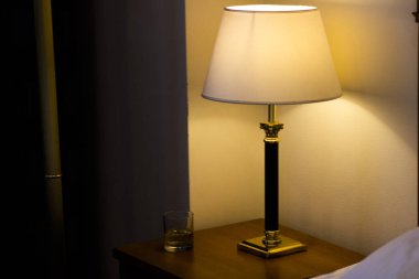 Komodinin üzerinde beyaz bir gölge olan bir lamba.