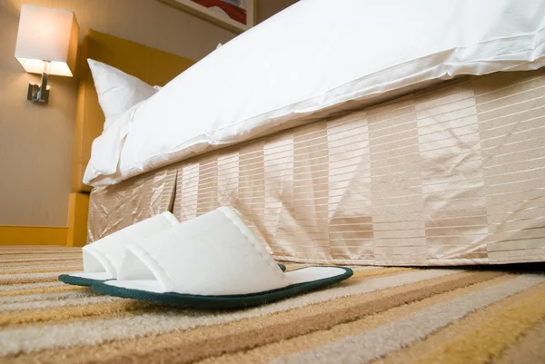 Тапочки и кровать в номере отеля — стоковое фото