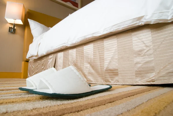 Chinelos e cama em um quarto de hotel — Fotografia de Stock