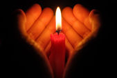ruce držící hořící svíčku ve tmě