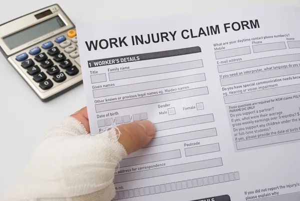 Mão machucada segurando um formulário de pedido de lesão no trabalho — Fotografia de Stock
