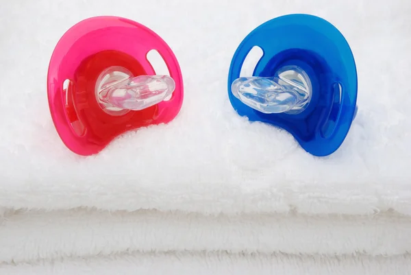 Red and blue pacifiers on white towel — Stock Photo, Image